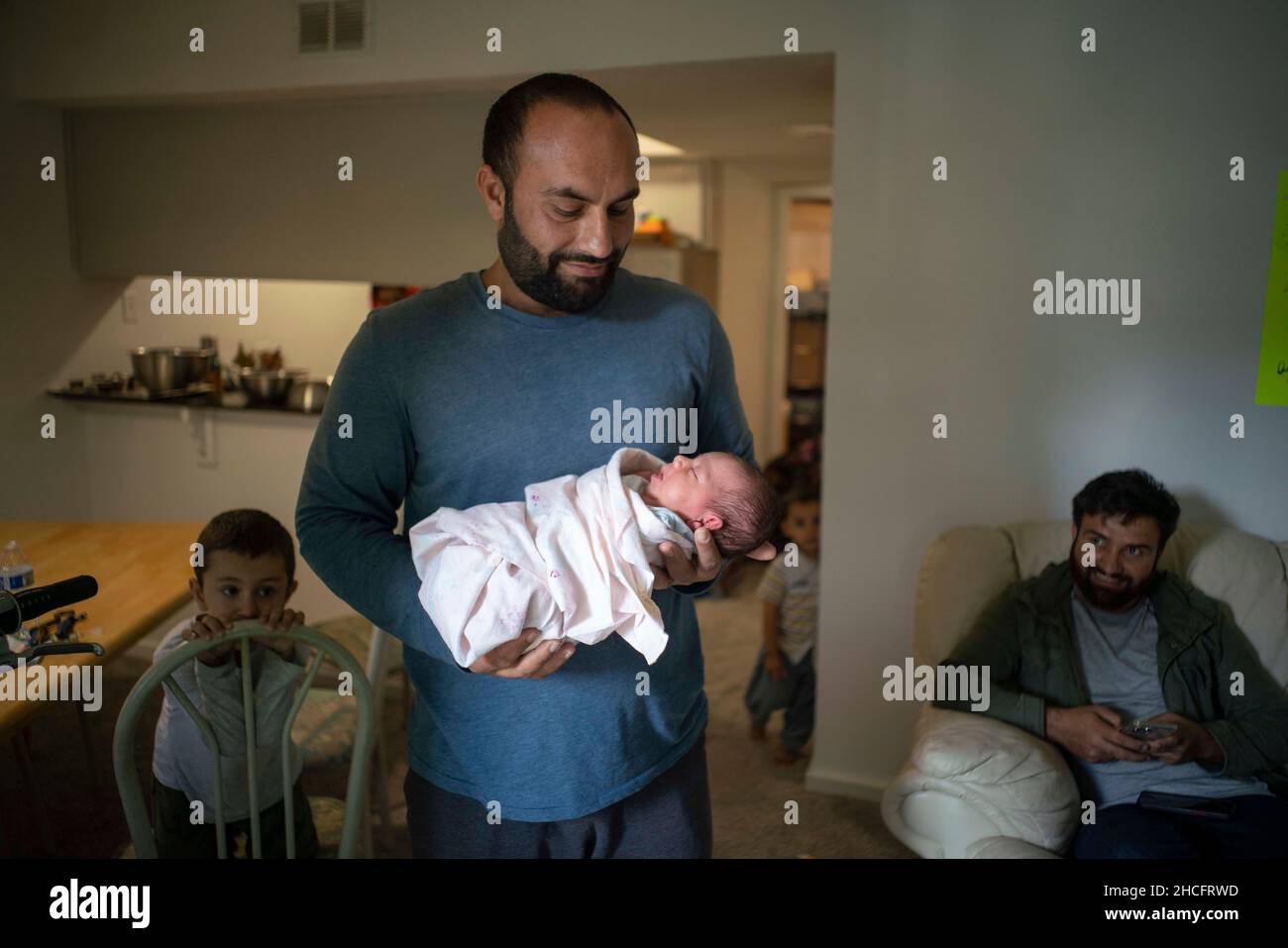 Austin Texas USA, Dezember 2021: Ein Mann hält das 4 Tage alte Mädchen seiner Schwester, das vorübergehend bei seiner Familie in der Wohnung wohnt, in die sie gerade eingezogen sind. Flüchtlinge, die vor den Unruhen in Afghanistan fliehen, werden weiterhin in Texas umgesiedelt, wobei viele alleinerziehende Männer und große Familien mit Kindern in Wohnungen in ganz Austin ziehen. Religiöse und andere gemeinnützige Gruppen haben sich verstärkt, um die Bemühungen zur Einrichtung von Häusern für Hunderte von Flüchtlingen zu koordinieren. ©Bob Daemmrich Stockfoto