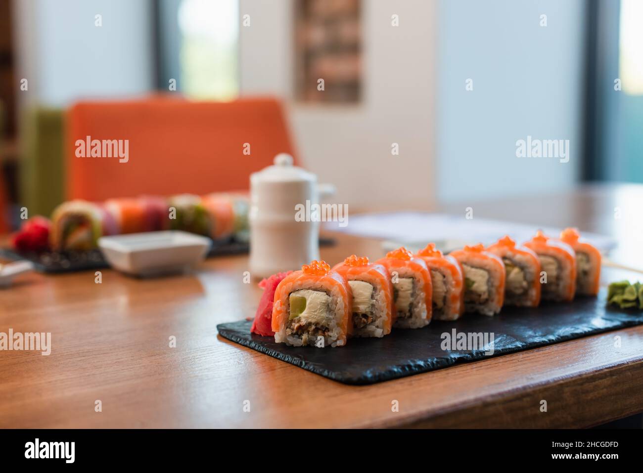 Selektiver Fokus des Tellers mit Sushi-Rollen in der Nähe von Sojasauce-Topf und Schüssel auf verschwommenem Hintergrund Stockfoto
