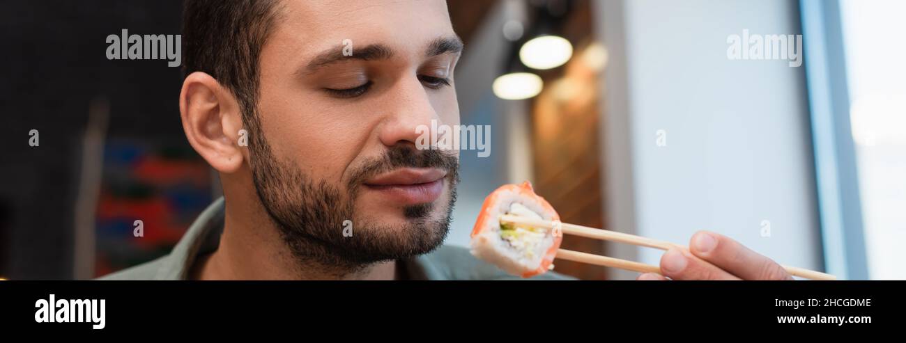 Junger Mann mit Essstäbchen mit köstlicher Sushi-Rolle, Banner Stockfoto