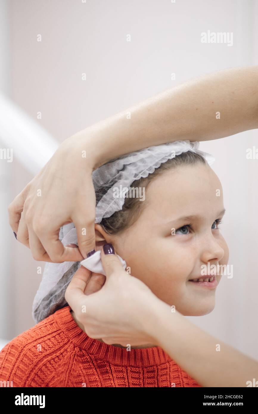 Nahaufnahme von Krankenschwesternhänden, die die Ohren des kleinen Mädchens mit Antiseptikum, Alkohol oder Desinfektionsmittel abwischen, um sich für das Ohrpiercing im Kosmetologiebüro vorzubereiten Stockfoto