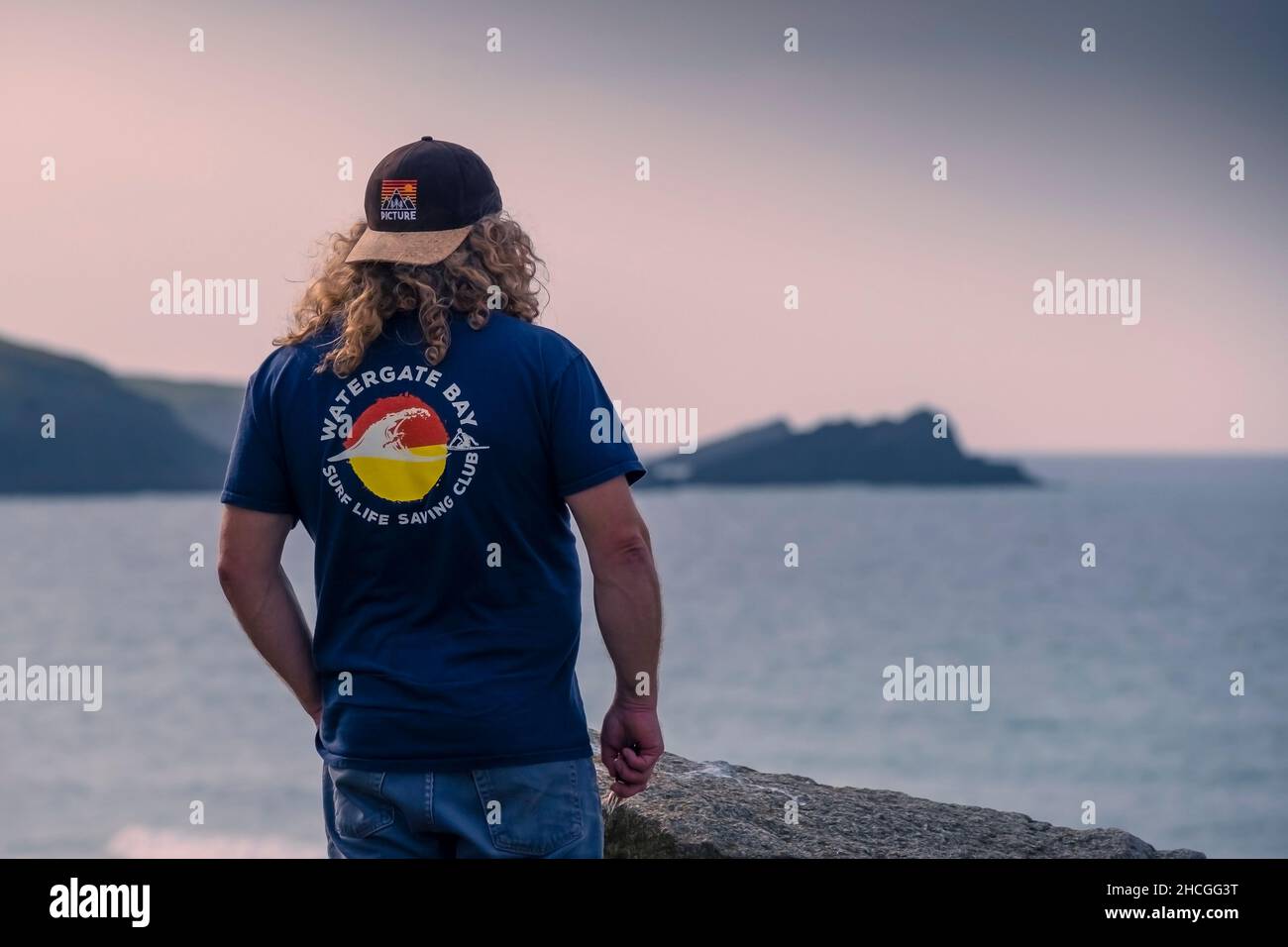 Abendlicht über einem Mann mit einem unverwechselbaren T-Shirt und Blick auf die Fistral Bay in Newquay in Cornwall. Stockfoto