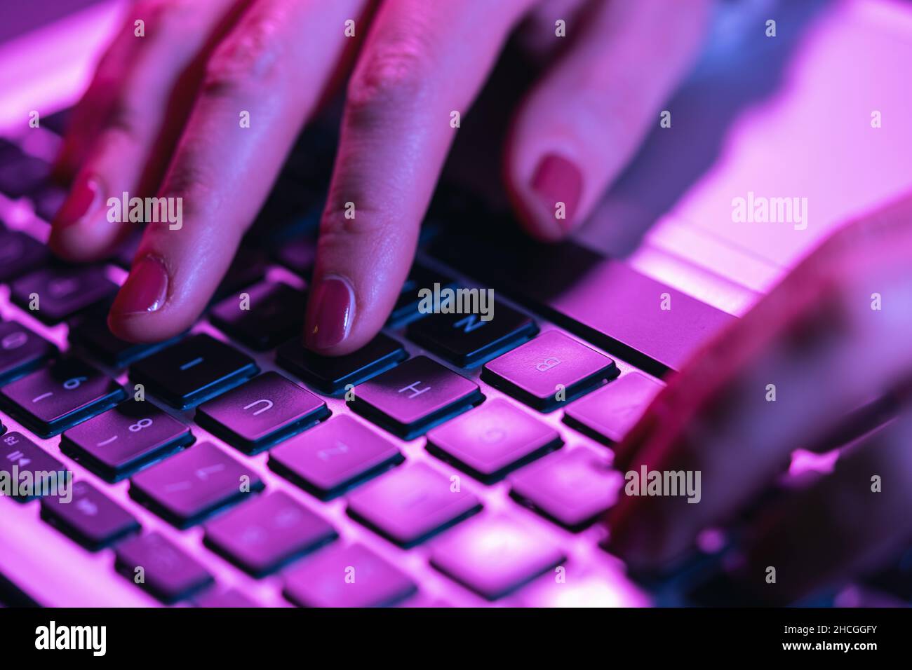 Nahaufnahme Frau Hände tippen auf Laptop-Tastatur, professionelle Online-Gamer Finger auf Notebook-Tastatur in Neon-Farbe, sitzen am Gaming-Schreibtisch Stockfoto