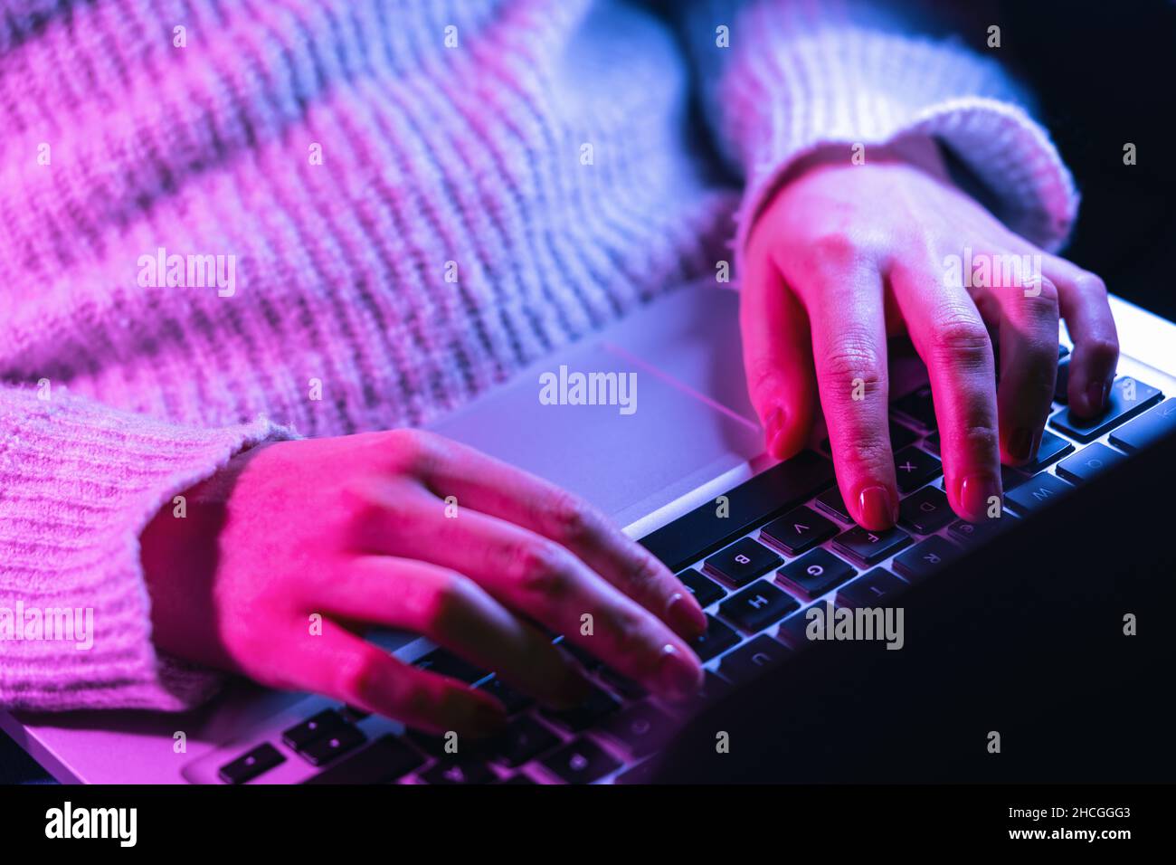 Nahaufnahme Frau Hände tippen auf Laptop-Tastatur, professionelle Online-Gamer Finger auf Notebook-Tastatur in Neon-Farbe, sitzen am Gaming-Schreibtisch Stockfoto