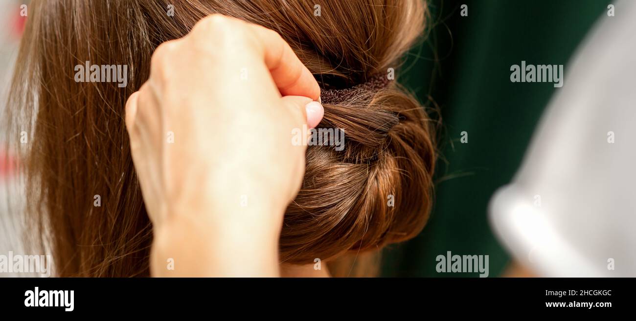 Friseurhands, die französische Frisur einer nicht erkennbaren jungen Brünette in einem Schönheitssalon drehen, Rückansicht, Nahaufnahme Stockfoto