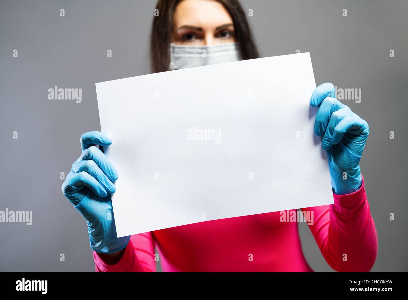 Frau in medizinischer Maske und Handschuhen, die leeres leeres leeres Papier in ihren Händen zeigt. Konzentrieren Sie sich auf ein Stück Papier. Verhindern Sie, dass andere von Corona COVID-19 und SARS COV 2 Stockfoto