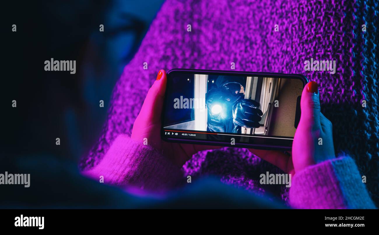 Frau, die sich einen Kriminalfilm auf einem Mobiltelefon mit imaginärem Videoplayer ansieht. Online-Film-Stream mit Smartphone. Stockfoto