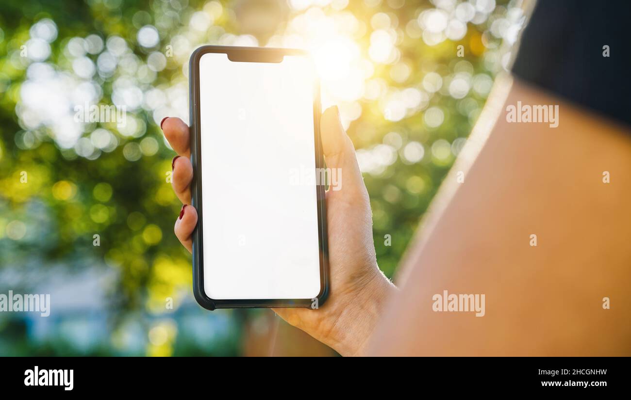 Mockup Bild von Frauen Hände halten schwarzes Smartphone mit weißem leeren Bildschirm auf einem im Park Stockfoto
