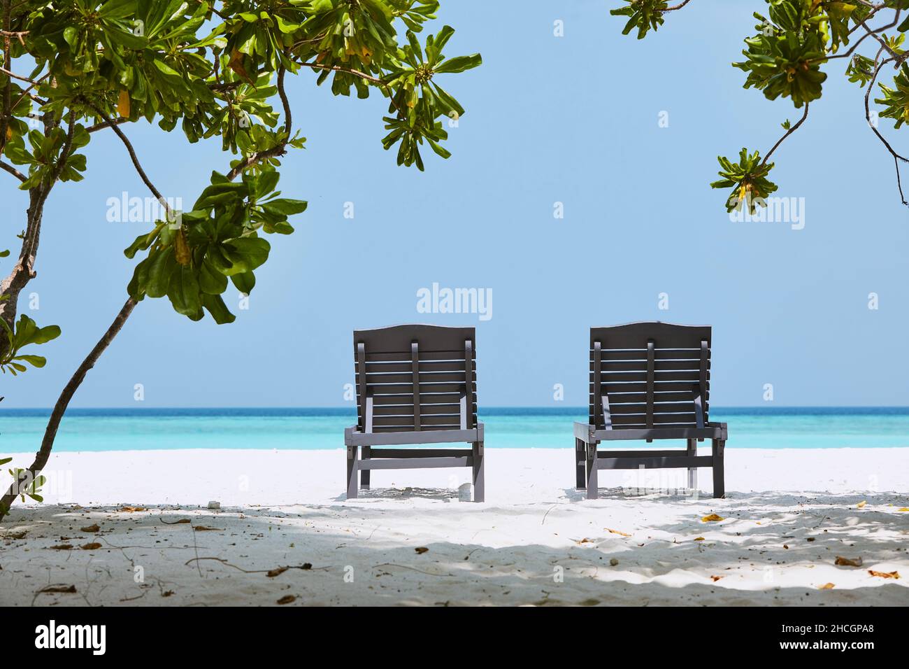 Rückansicht auf zwei leeren Holzliegen am idyllischen Sandstrand gegen das türkisfarbene Meer. Stockfoto
