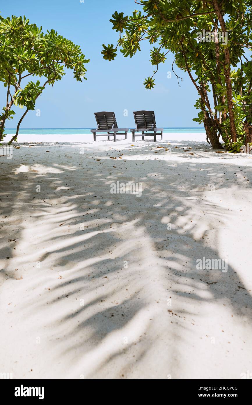 Rückansicht auf zwei leeren Holzliegen am idyllischen Sandstrand gegen das türkisfarbene Meer. Stockfoto