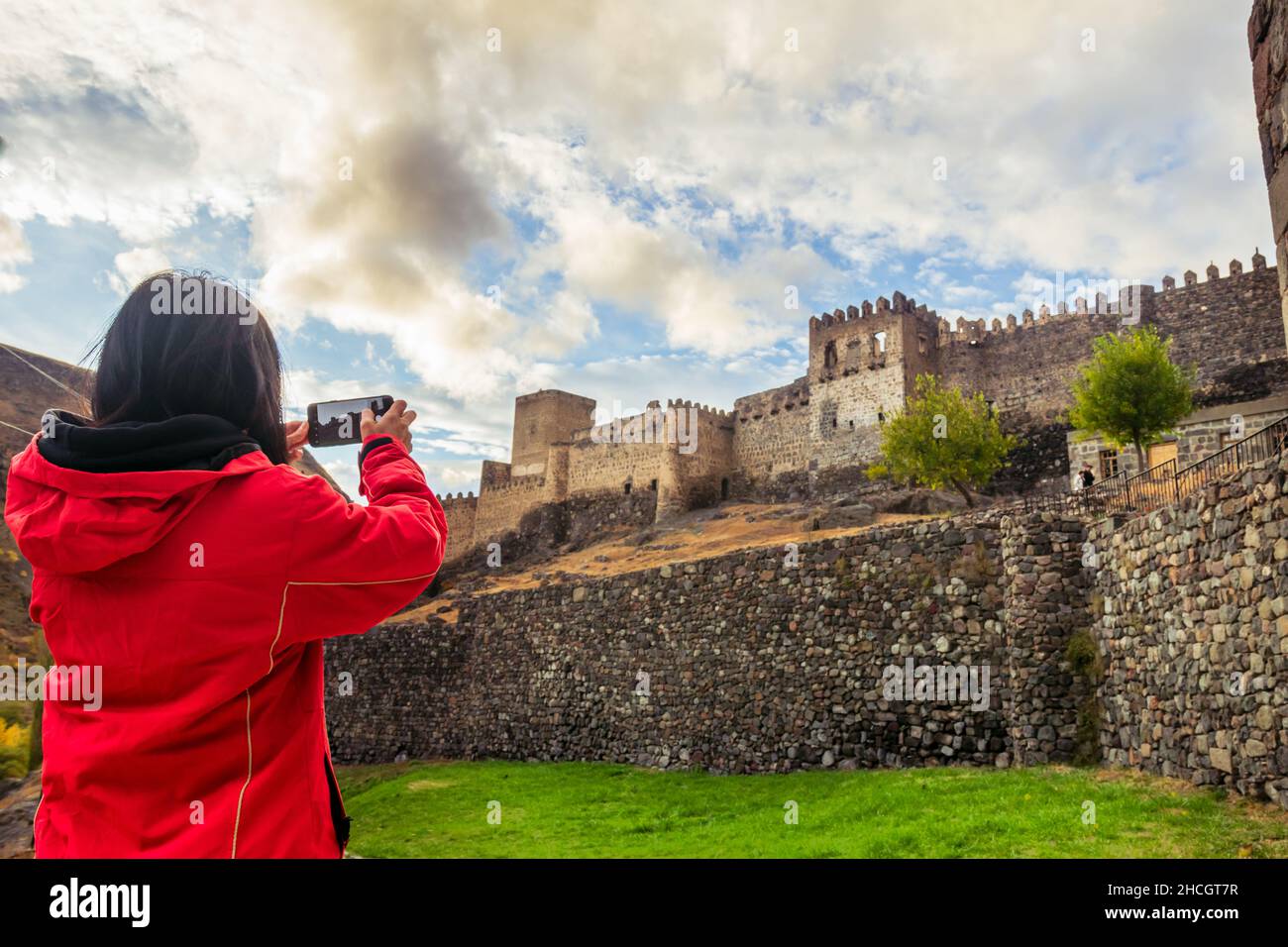 Verlieren Sie eine Frau, die am bewölkten Tag das Mobiltelefon vor der historischen Festung der Sehenswürdigkeiten hält. Mobile Fotografie und Urlaubsfoto auf Socia Stockfoto