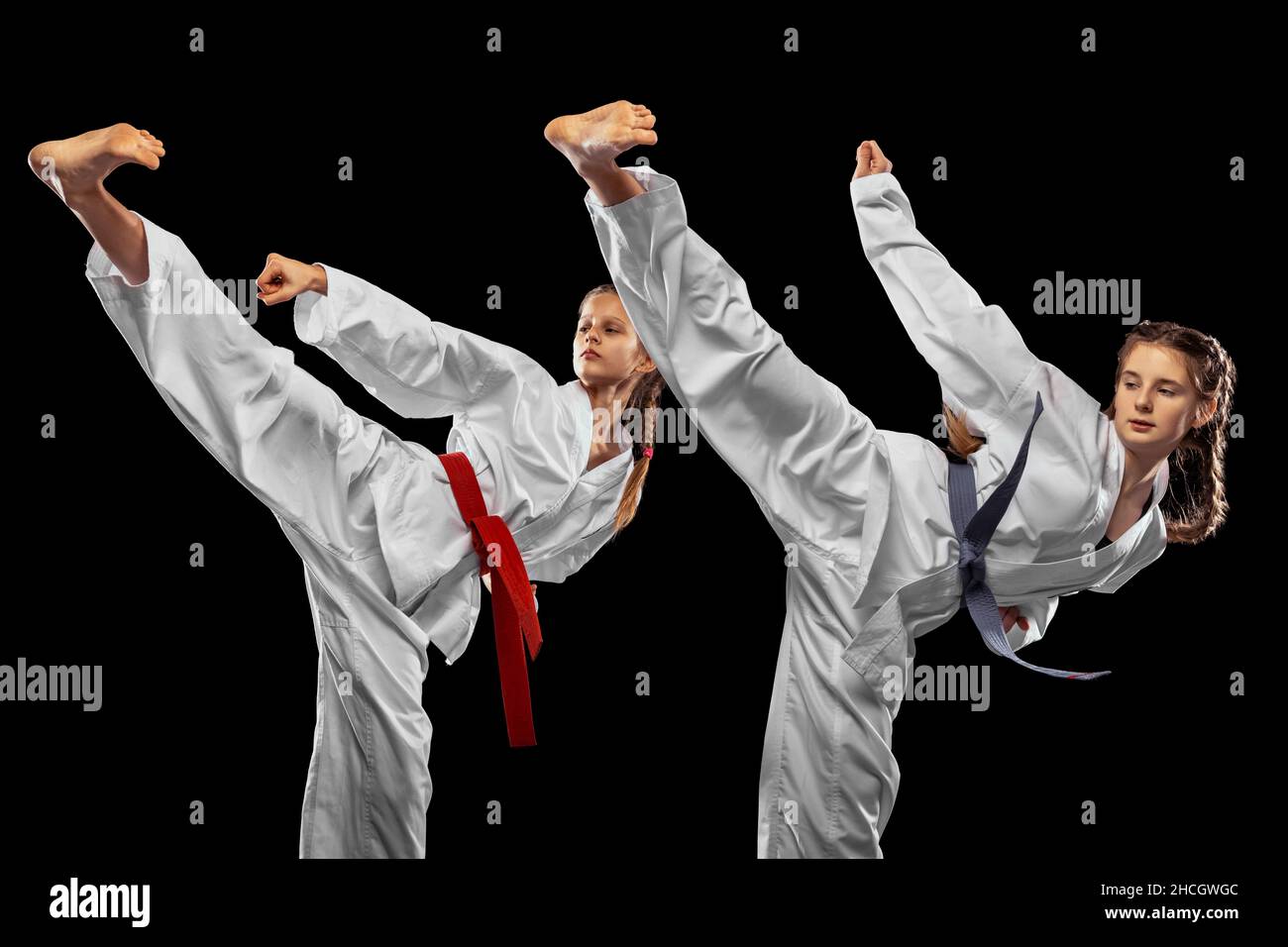 Zwei junge Mädchen, Teenager, Taekwondo-Athleten trainieren gemeinsam isoliert auf dunklem Hintergrund. Konzept von Sport, Bildung, Fähigkeiten Stockfoto