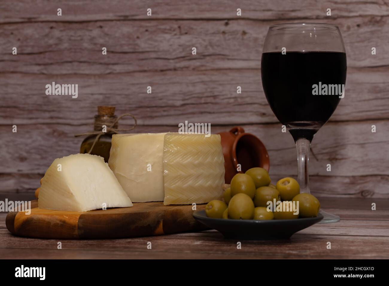 Geräucherter Käse, geschnitten mit einem Glas Rotwein, gefüllten Oliven und nativem Olivenöl extra auf einem Holztisch Stockfoto