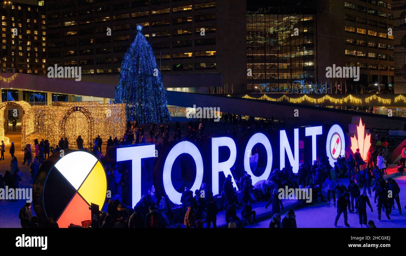 Menschen am Toronto 3D Schild am Nathan Phillips Platz. Der große Weihnachtsbaum und andere Lichter sind im Hintergrund zu sehen. 29. Dezember 2021 Stockfoto