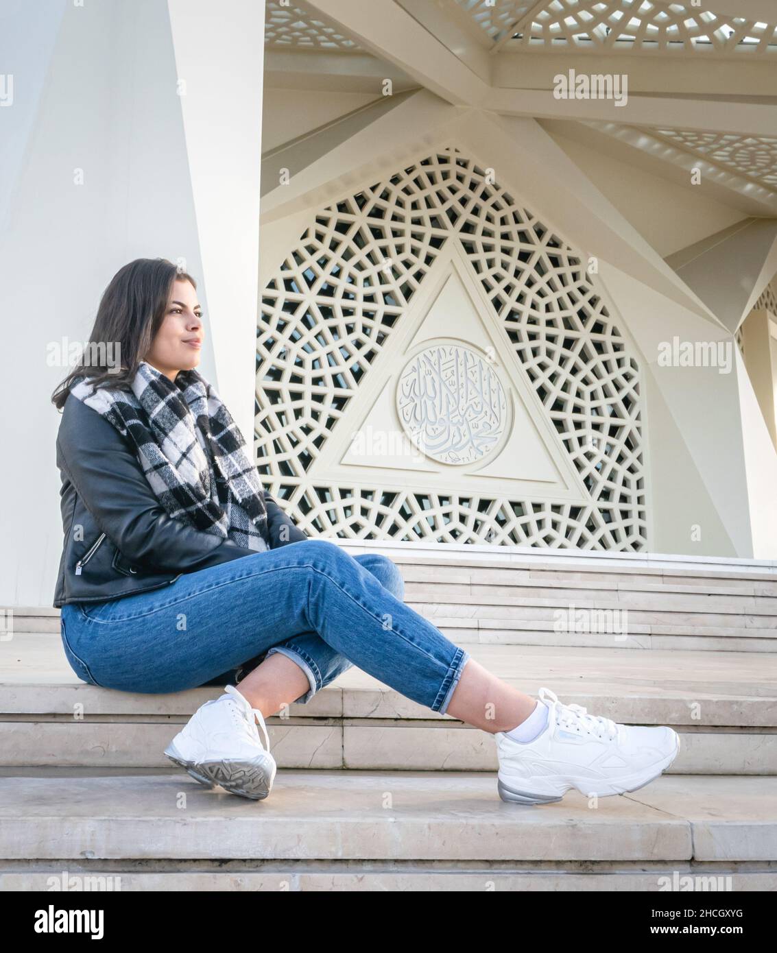 Weibliche Person in legerer Kleidung sitzt auf der Treppe am Eingang der einzigartigen modernen marmara Universitätsmoschee. Touristenattraktion in der Türkei. Stockfoto