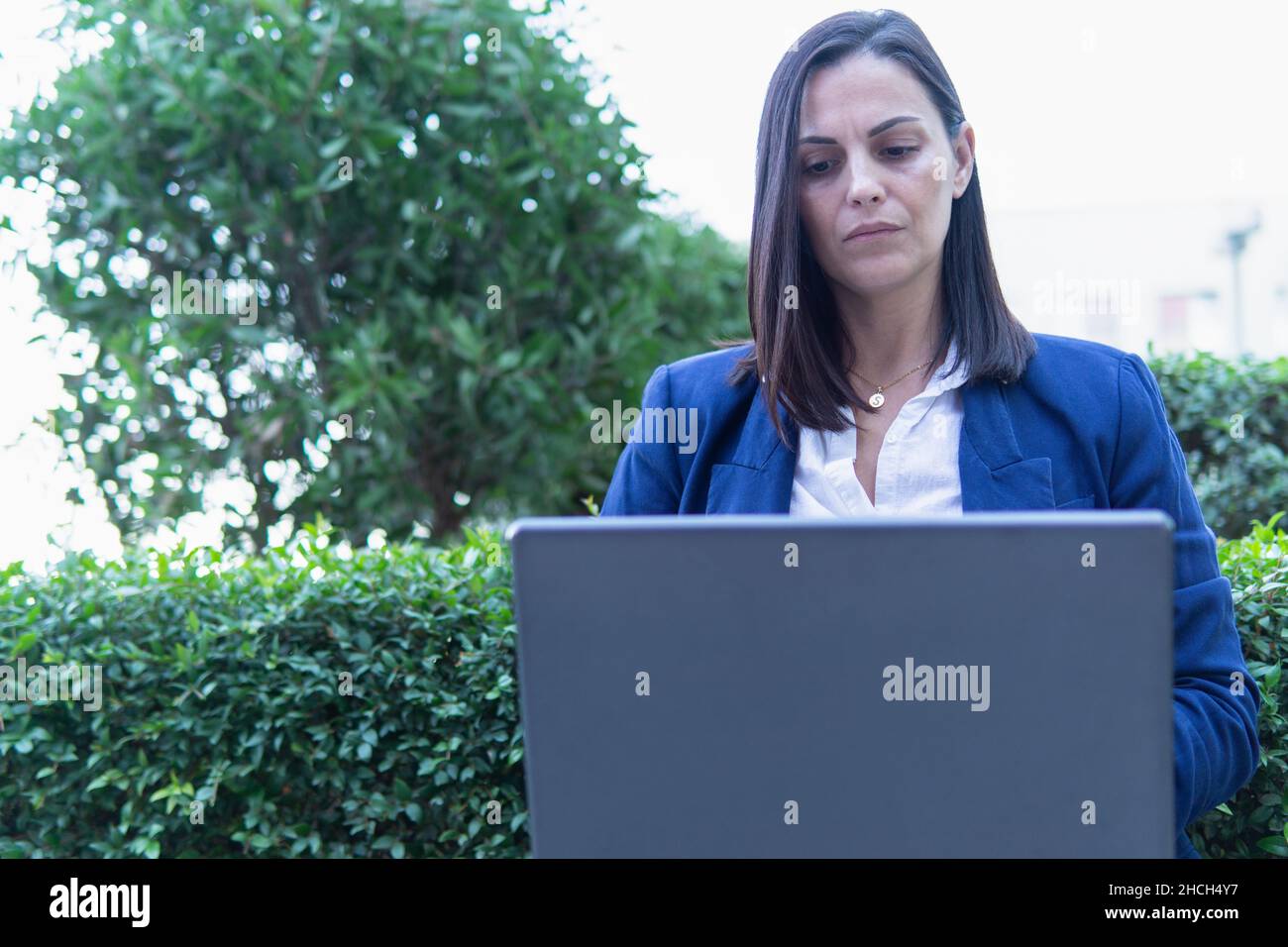 Schöne kaukasische Geschäftsfrau, die einen Laptop mit einer Tasse Kaffee vor einem Bürogebäude sitzt. Stockfoto