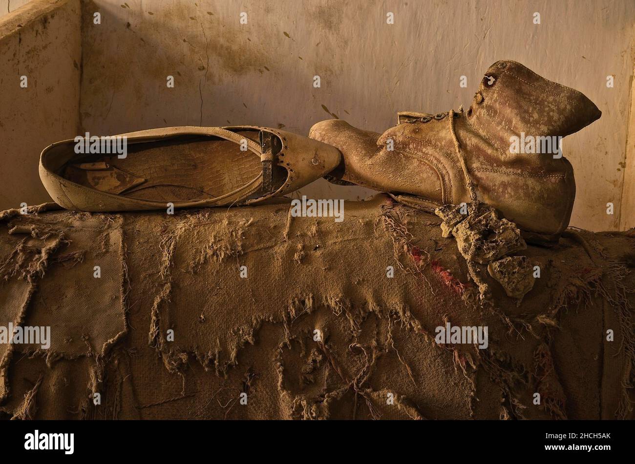 Damenschuh und Arbeitsschuh stehen sich auf einer zerrissenen Jute-Tasche gegenüber Stockfoto