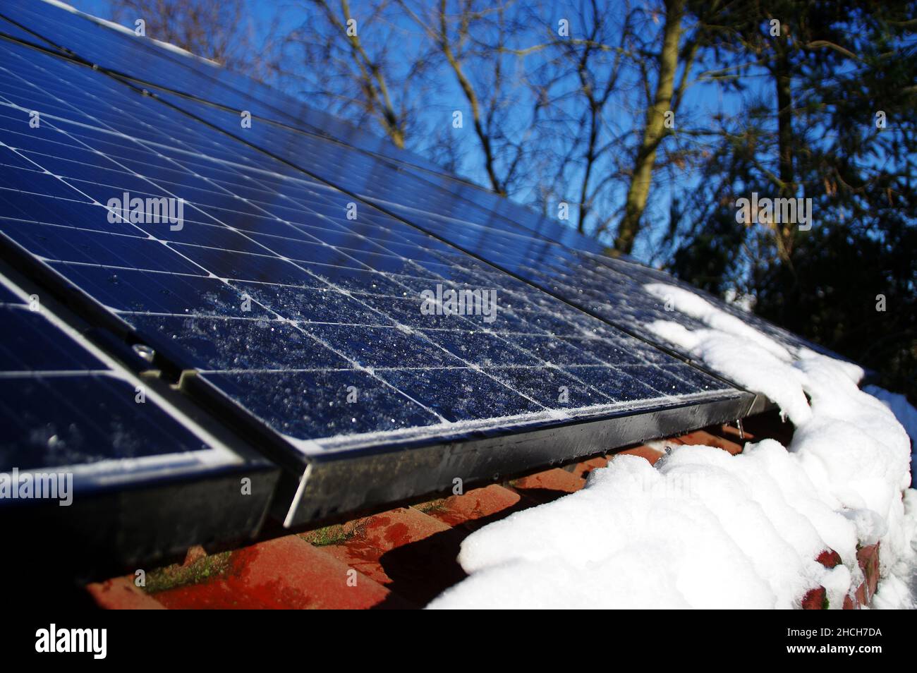 Sonnenkollektoren von Schnee und Eis bedeckt. Photovoltaikanlage auf dem Hausdach. Wintersaison an einem sonnigen Tag. Alternative PV-Energie pro Stockfoto