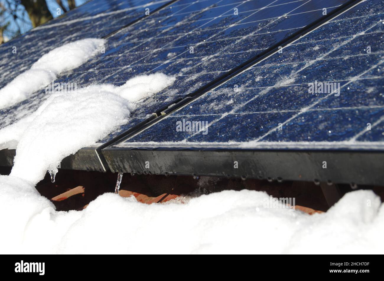 Sonnenkollektoren von Schnee und Eis bedeckt. Photovoltaikanlage auf dem Hausdach. Wintersaison an einem sonnigen Tag. Alternative PV-Energie pro Stockfoto