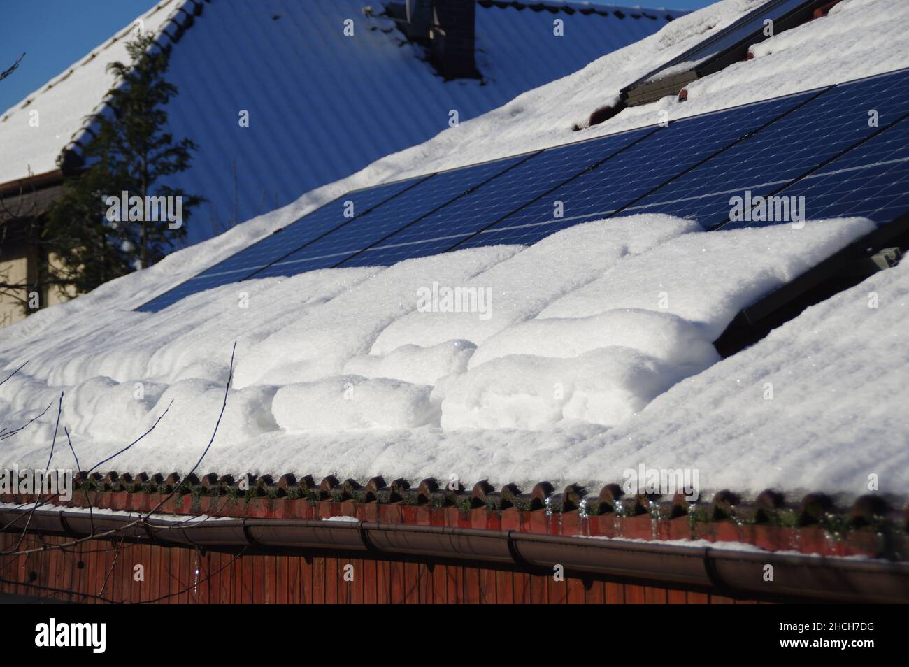 Sonnenkollektoren von Schnee bedeckt. Photovoltaikanlage auf dem Hausdach während der Wintersaison an einem sonnigen Tag. PV-Energieerzeugung. Niedrig p Stockfoto