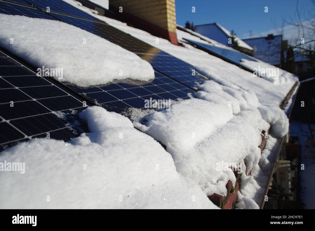 Sonnenkollektoren von Schnee bedeckt. Photovoltaikanlage auf dem Hausdach während der Wintersaison an einem sonnigen Tag. PV-Energieerzeugung. Niedrig p Stockfoto