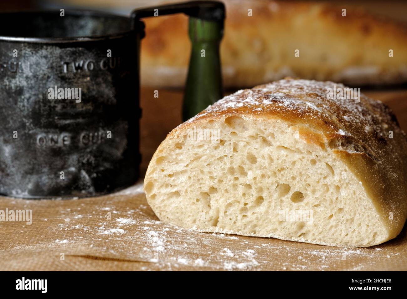 Ein frisch geschnittenes Brot aus hausgemachtem, handwerklichem Weißbrot auf einem Backblech. Der Mehlsichter, der zum Stauben des Brotes verwendet wurde, befindet sich im Hintergrund. Stockfoto