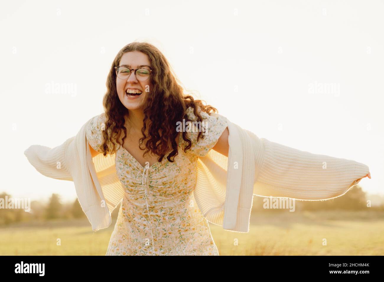 Kaukasisches Mädchen, das an einem sonnigen Tag mit weit geöffneten Händen auf einem Feld lacht - Konzept des Glücks Stockfoto