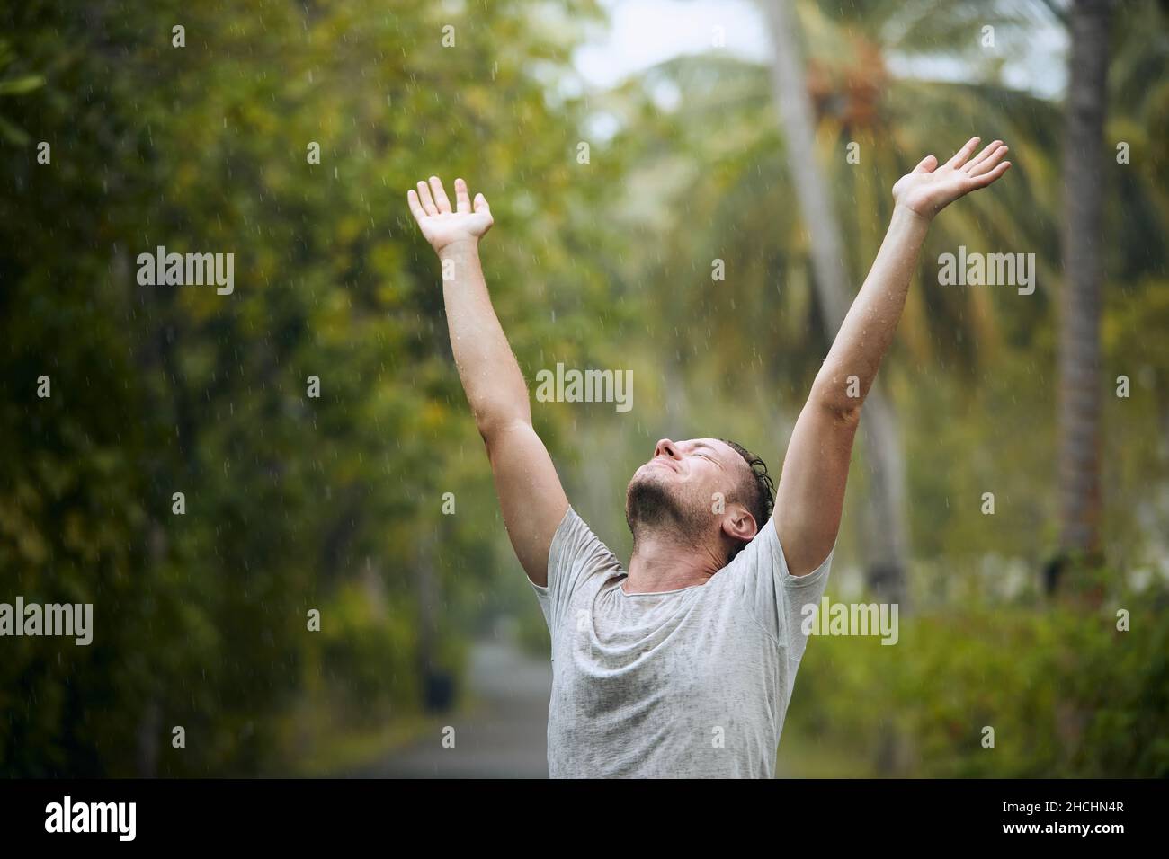 Porträt eines durchnäßten Mannes mit geschlossenen Augen, der starken Regen in der Natur genießt. Stockfoto