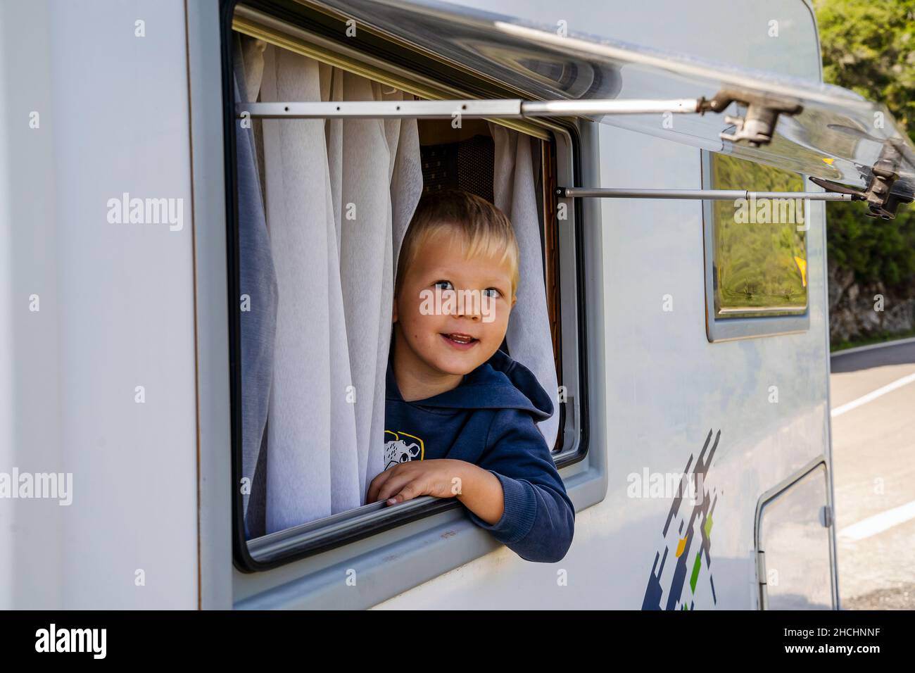 Glücklicher kleiner Junge, der durch das Fenster des Wohnmobils schaute, der entlang der Straße, Portugal, geparkt war Stockfoto