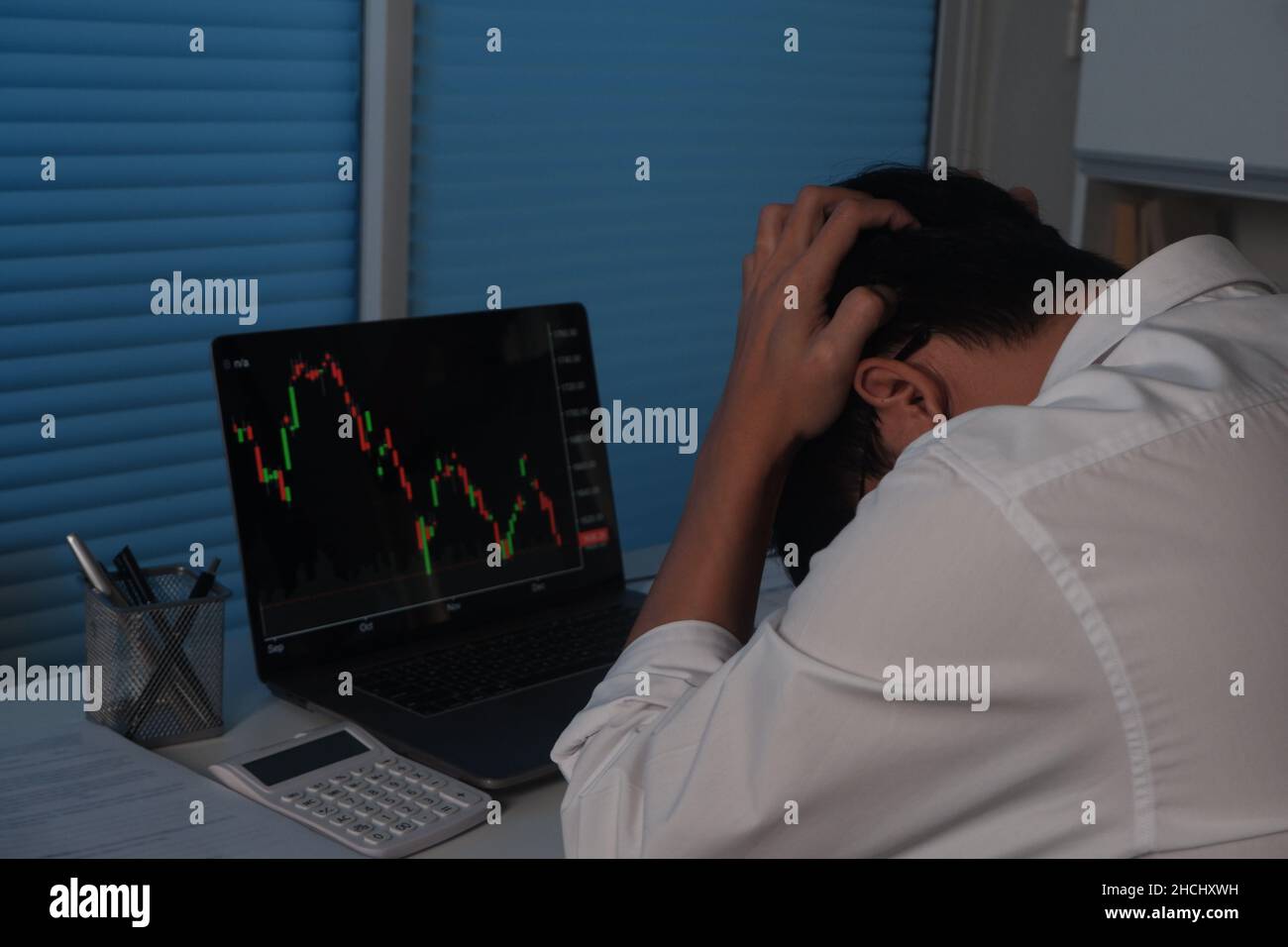Trauriger Geschäftsmann, der nachts arbeitet, vor dem Laptop-Bildschirm, der Handelsgraph, Bitcoin, Börse zeigt Stockfoto