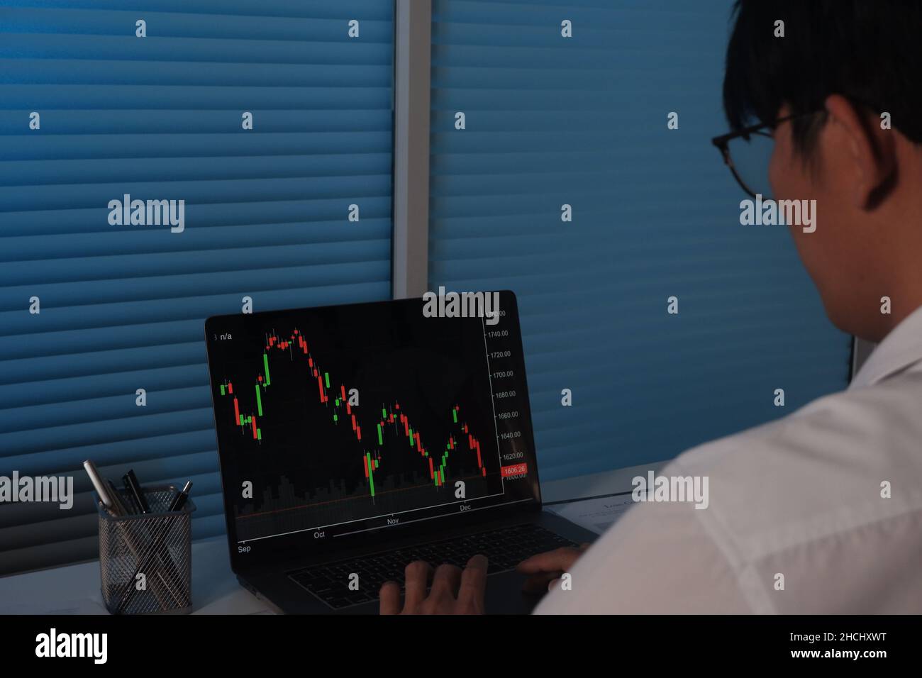 Trauriger Geschäftsmann, der nachts arbeitet, vor dem Laptop-Bildschirm, der Handelsgraph, Bitcoin, Börse zeigt Stockfoto