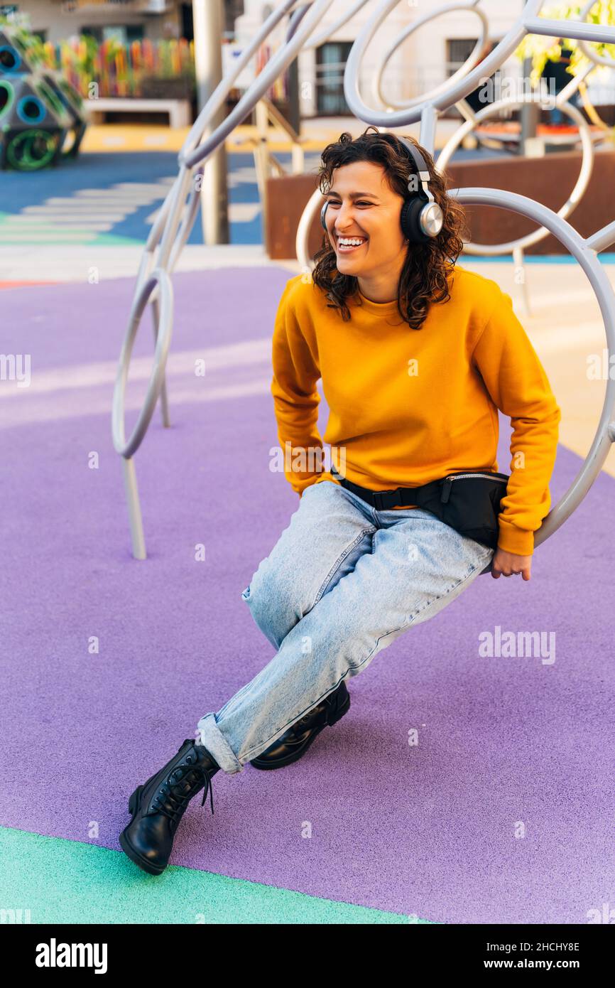 Fröhliche junge Frau, die auf dem Spielplatz sitzt Stockfoto