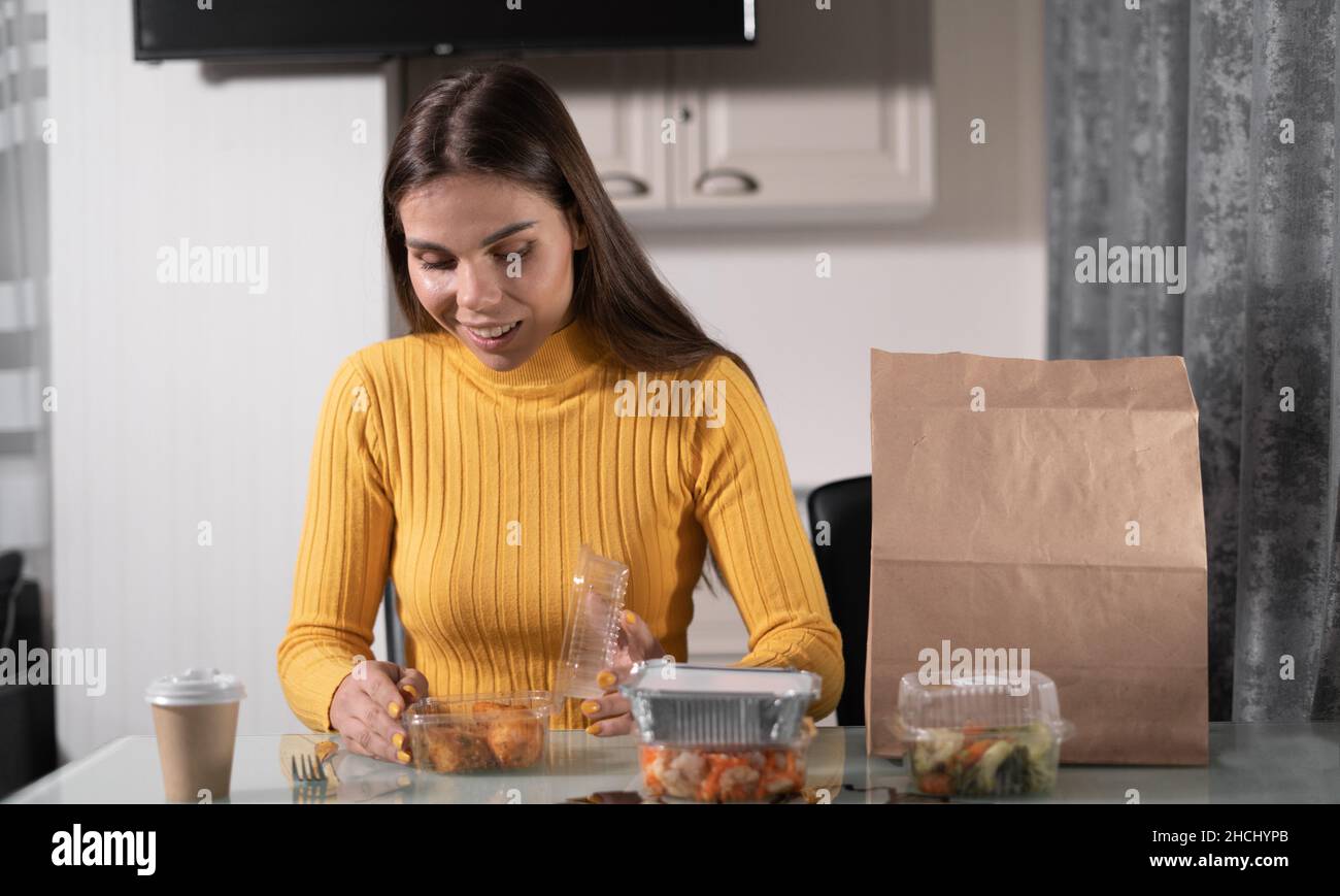 Ein schönes kaukasisches Mädchen sitzt am Tisch zu Hause allein am Abend und wird das Abendessen aus Einweg-Gerichte haben. Gebratene Hühnerbeine Stockfoto