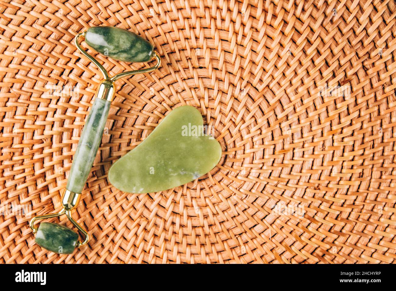 Jade Gesichtswalze und Gua Sha Werkzeug auf natürlichen Stroh Hintergrund. Gesichtsmassage-Set für die Lifting-Massage-Therapie aus Natursteinen, persönlicher Ski Stockfoto