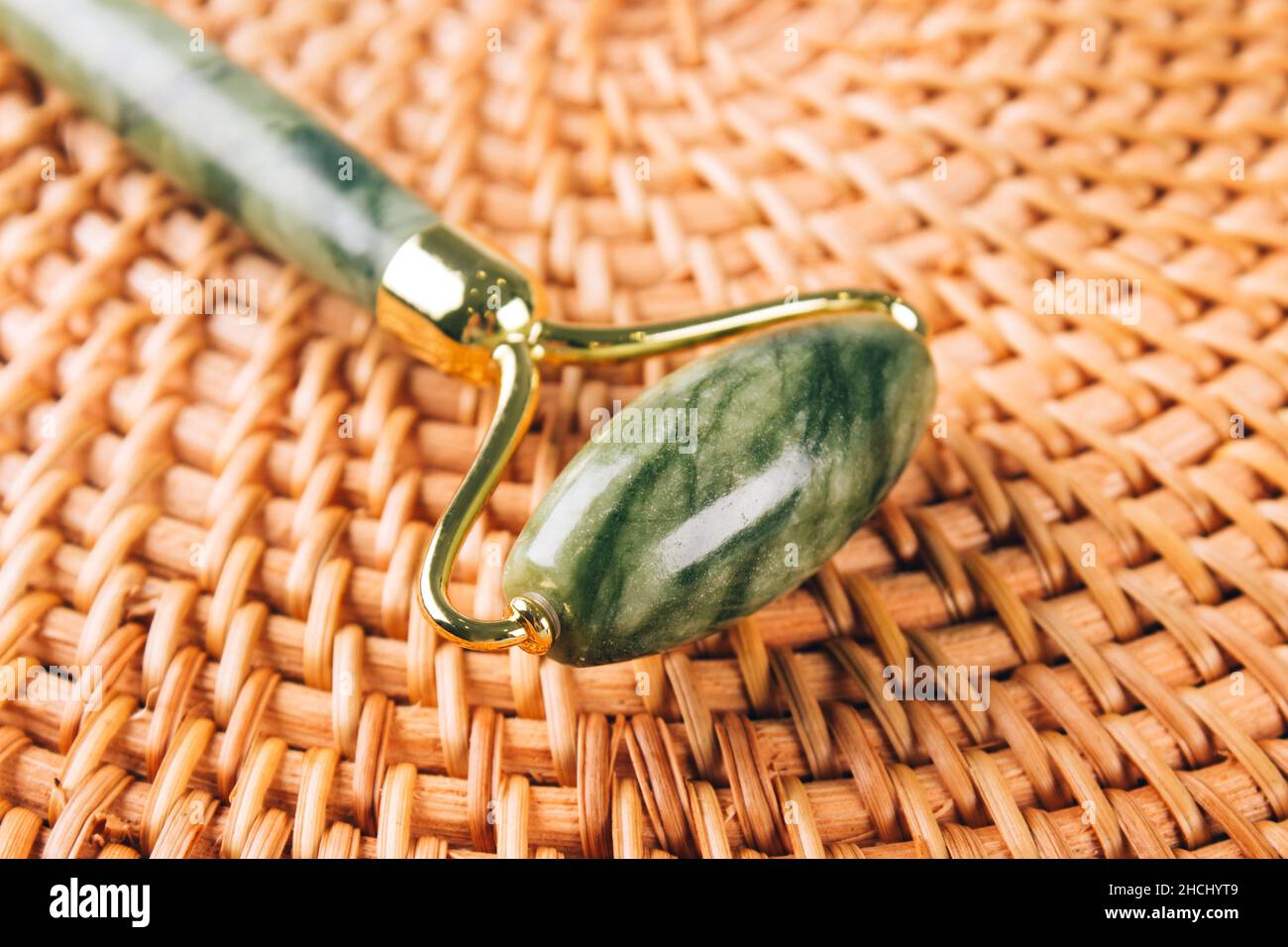 Nahaufnahme der Jade-Gesichtswalze und des Gua Sha-Werkzeugs auf natürlichem Strohgrund. Gesichtsmassage-Set für die Lifting-Massage-Therapie aus natürlichem sto Stockfoto