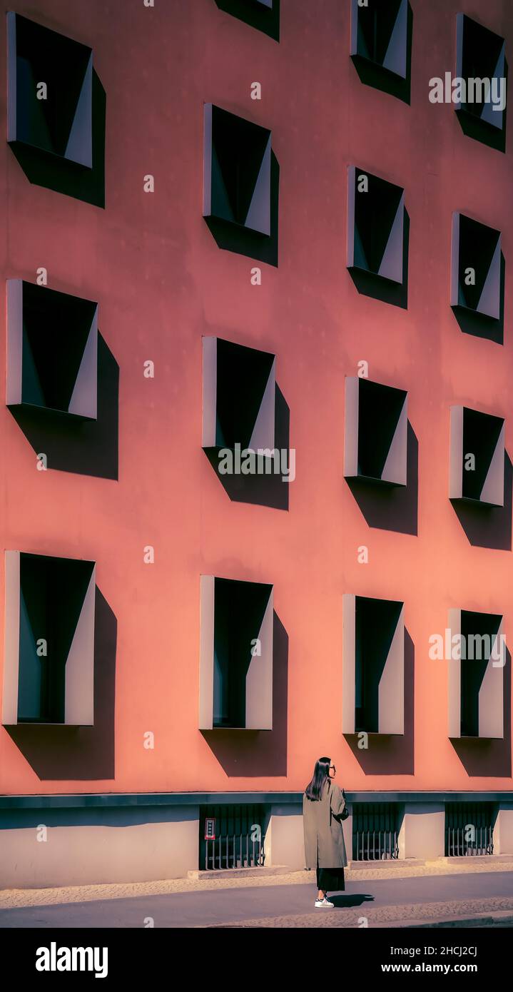 Der Mensch geht vorbei an puristischer zeitgenössischer Gebäudefassade mit systematischem Gitter aus einheitlichen Fenstern. Berlin Mitte Stockfoto