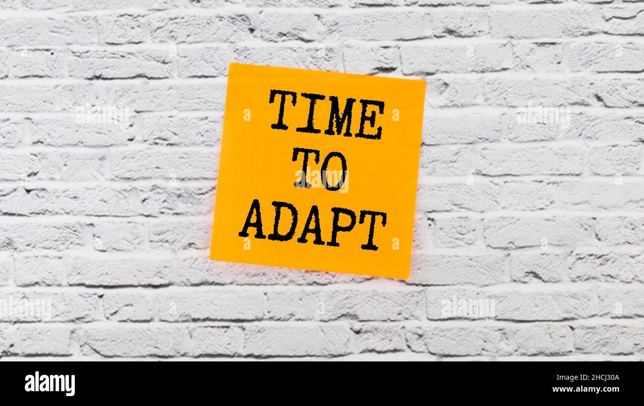 Weiße Note mit Aufschrift 'Time to Adapt' auf schönem gelben Hintergrund, farbigen Büroklammern, Metallstift, Kappe und Rechner. Geschäftskonzept. Stockfoto