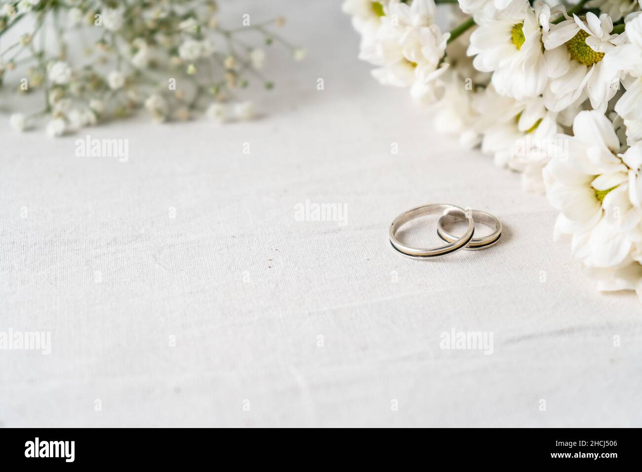 Ein Paar Eheringe auf einer weißen Oberfläche mit schönen weißen Blüten. Engagement und Liebe Konzept. Kopierbereich, differenzieller Fokus. Stockfoto