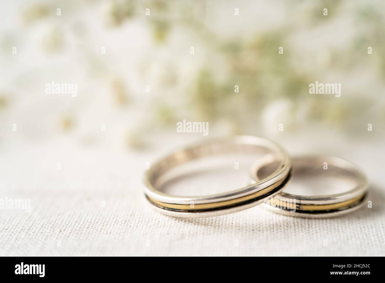 Ein Paar Eheringe auf einer weißen Oberfläche mit schönen weißen Blüten. Engagement und Liebe Konzept. Kopierbereich, differenzieller Fokus. Stockfoto