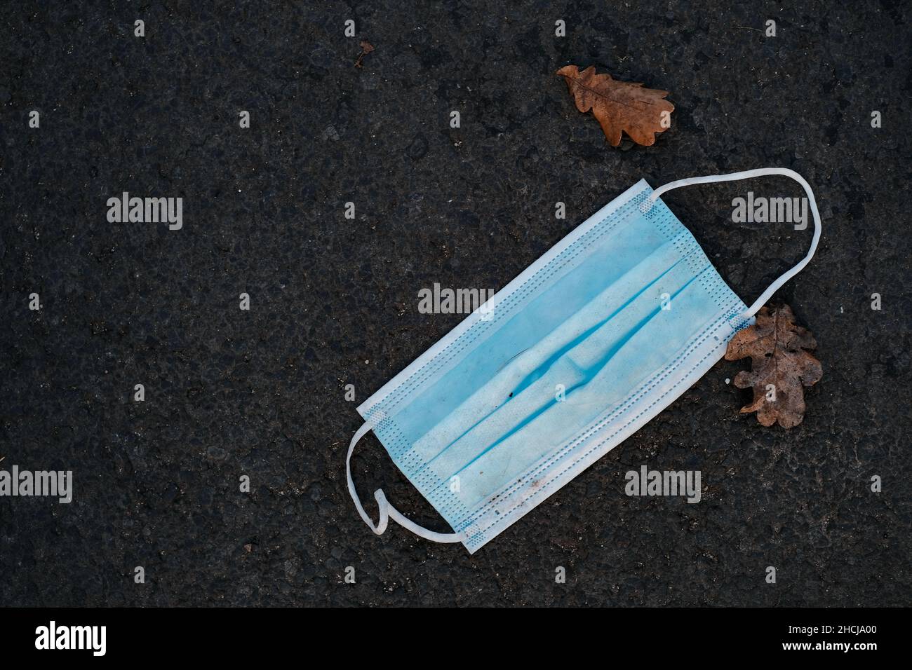 Arznei-Maske, die auf dem Asphalt neben zwei Herbstblättern liegt Stockfoto