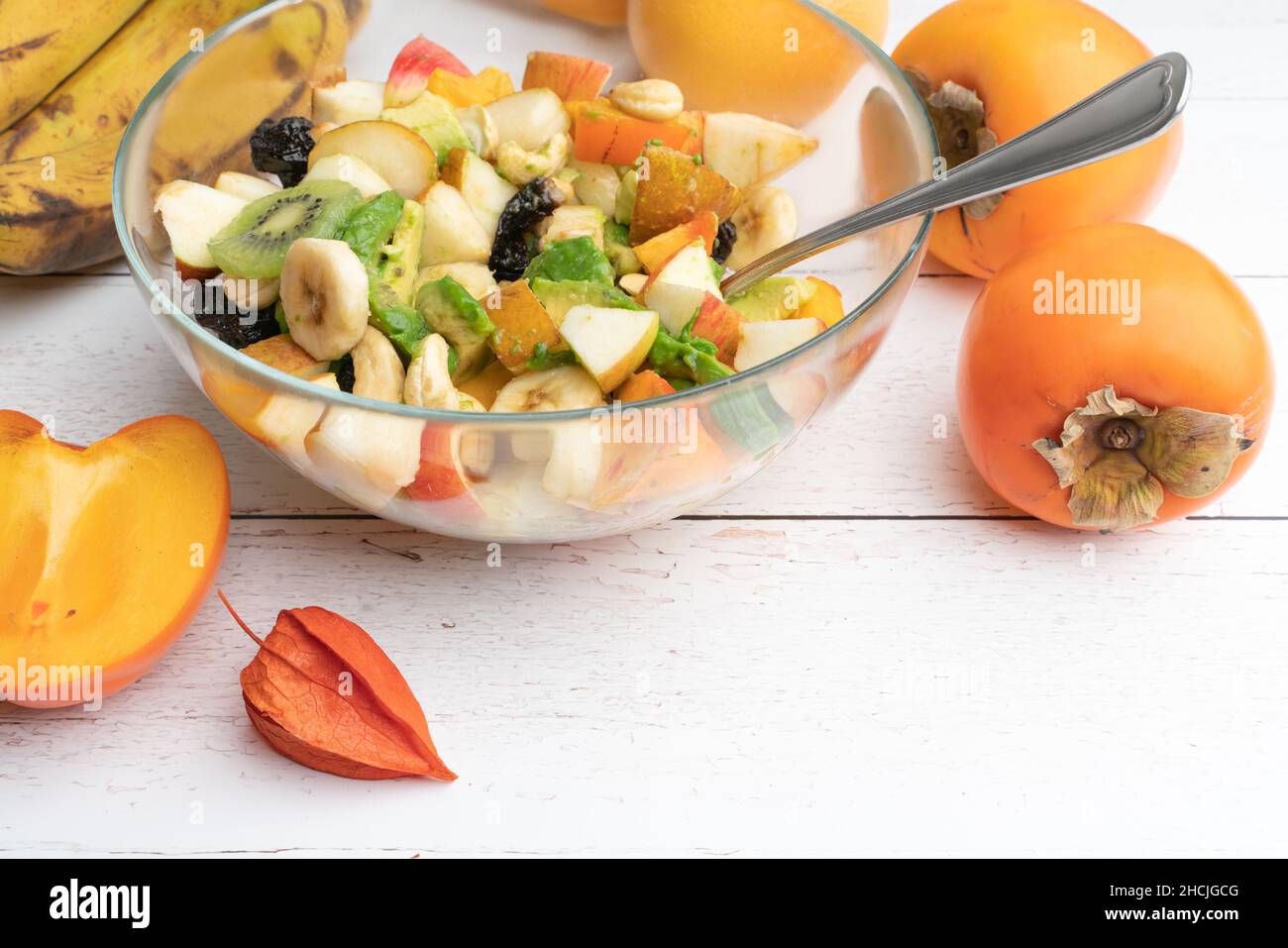 Studioaufnahme einer Glasschüssel mit frisch zubereitetem Obstsalat auf einem weißen Holztisch. Gesunde Ernährung Konzept. Vegetarische Gerichte. Vegane Rohkost Stockfoto