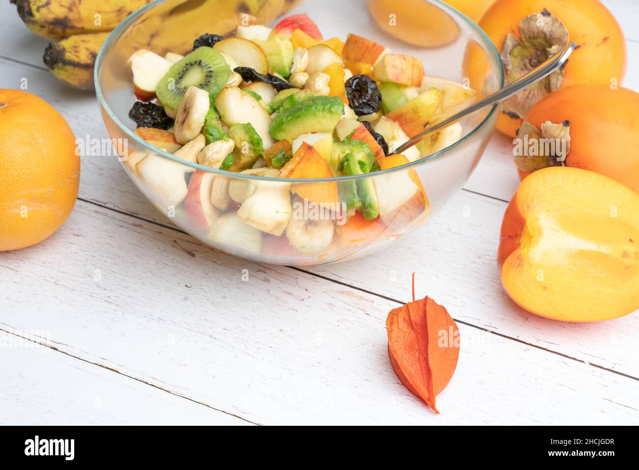 Studioaufnahme einer Glasschüssel mit frisch zubereitetem Obstsalat auf einem weißen Holztisch. Gesunde Ernährung Konzept. Vegetarische Gerichte. Vegane Rohkost Stockfoto