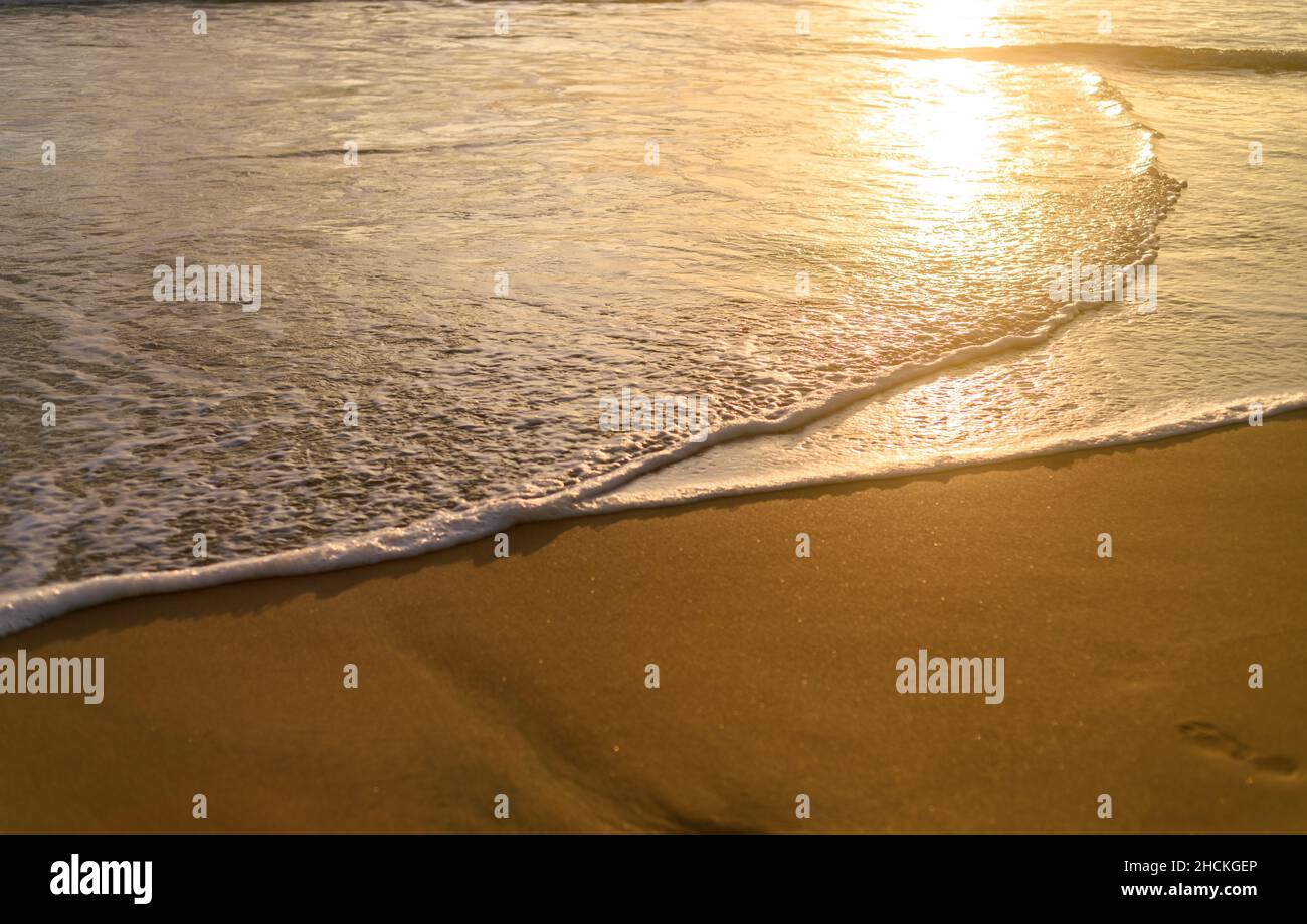 Das Licht des Sonnenuntergangs scheint auf den Wellen des Ozeans. Tropischer Sandstrand Sonnenuntergang Reflexion. Stockfoto