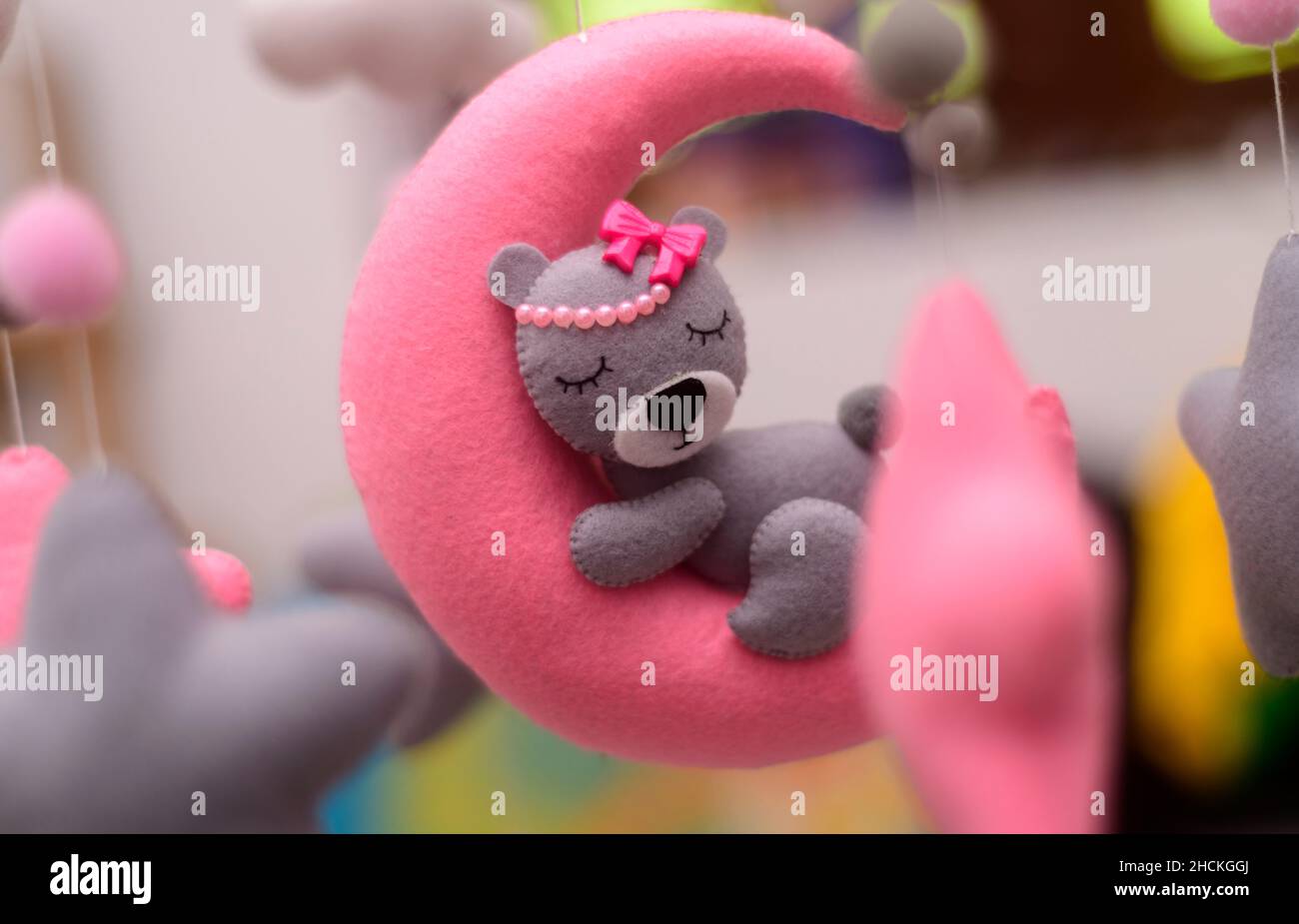 Babykrippe mobile Ornamente hängen aus nächster Nähe, grauer Wollfilz-Bär schläft auf einem rosa plüschtier-Mond, umgeben von Sternen. Stockfoto