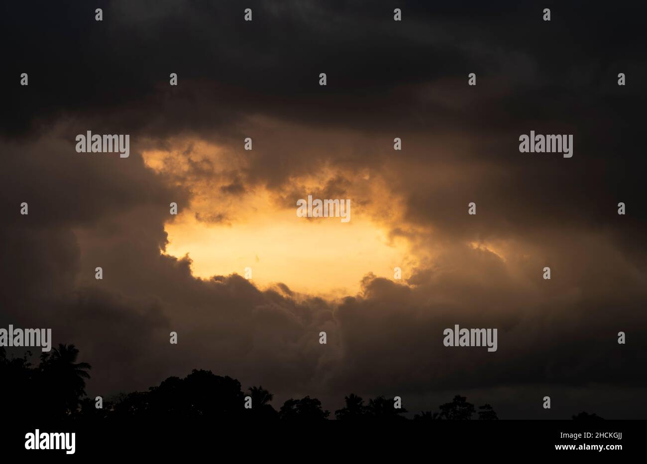 Am Abend sammeln sich dunkle Wolken am Horizont über der Baumgrenze. Glühender Sonnenschein, der durch die Wolkenformation geht. Stockfoto