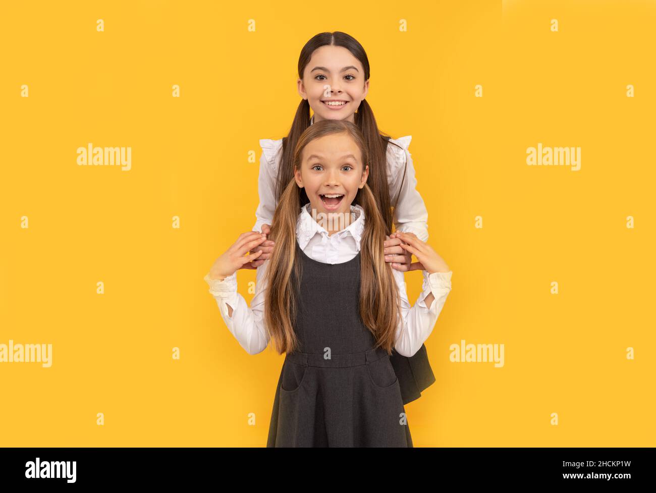 Glückliche Schulfreunde umarmen in formellen Uniformen gelben Hintergrund, Freundschaft Stockfoto