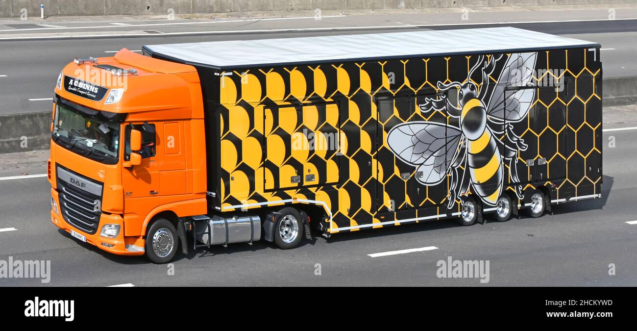 LKW-LKW für Spedition und beeindruckendes Grafikdesign in Seitenansicht des Anhängers mit großer Biene, die auf der britischen Autobahn mit Wabenhintergrund überzogen ist Stockfoto