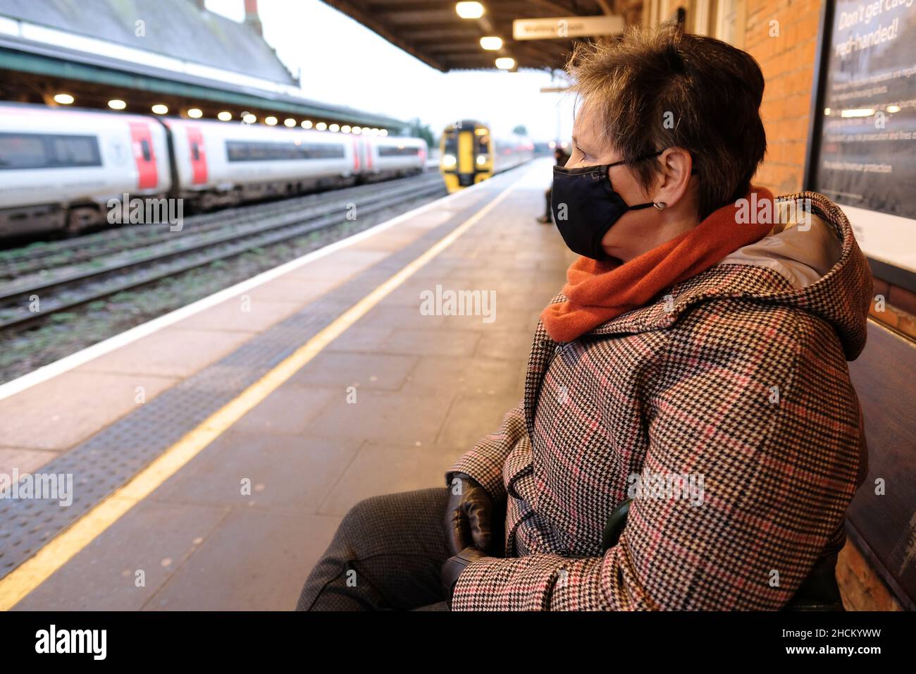 Zugfahrerin mit Covid-Gesichtsmask, die auf die Ankunft eines Zuges am Bahnsteig UK am 2021. Dezember wartet Stockfoto