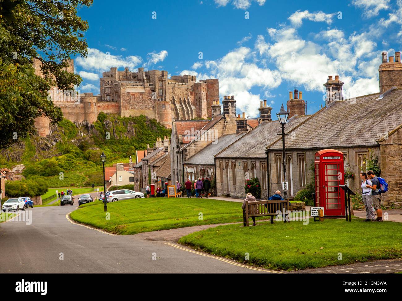 Touristen und Urlauber entlang der Hauptstraße im Dorf von Bamburgh Northumberland, England Großbritannien mit Bamburgh Castle im Hintergrund Stockfoto