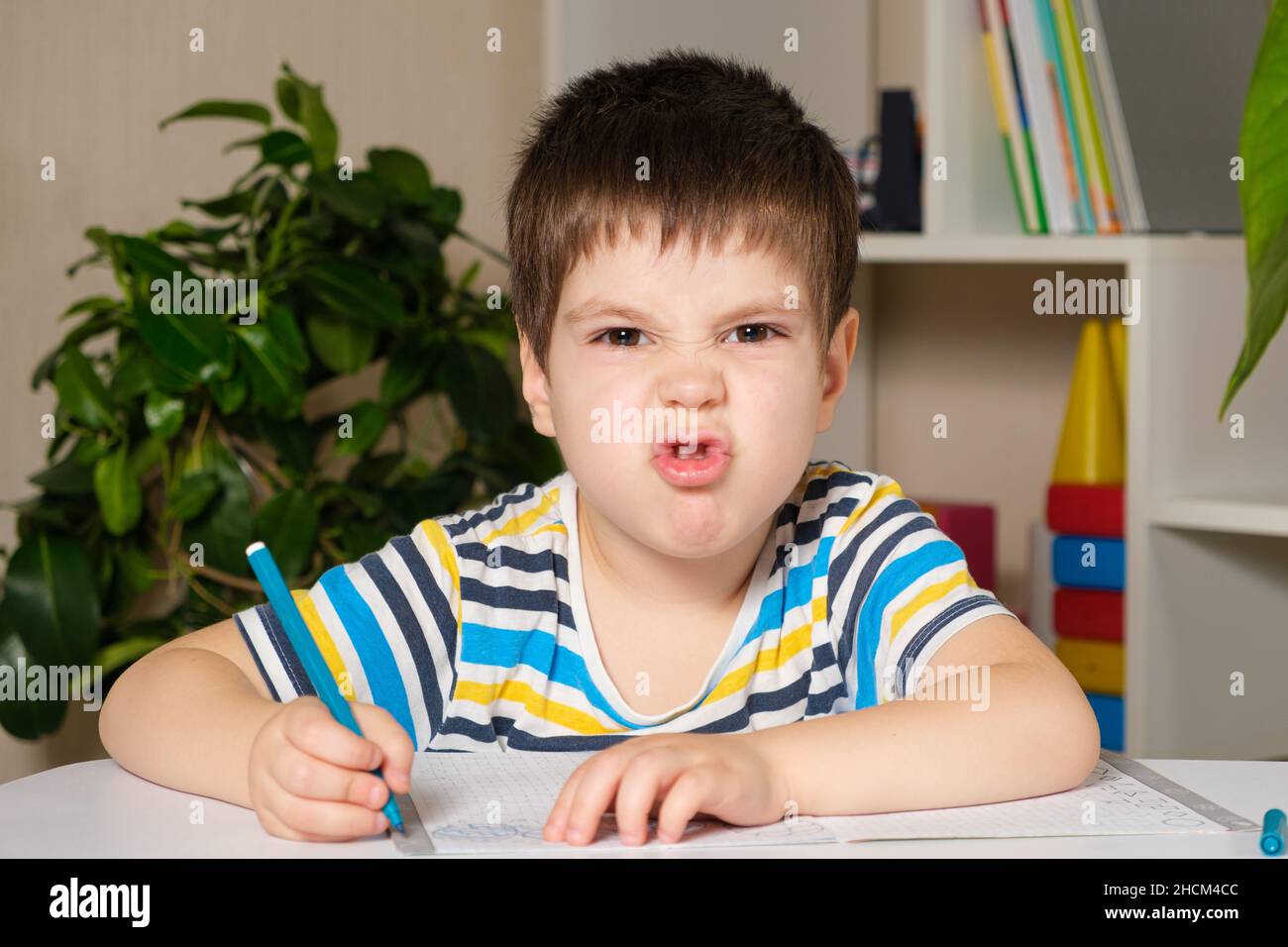 Ein hübscher Junge von 4 Jahren lernt schreiben, schaut in die Kamera und grimaces. Stockfoto