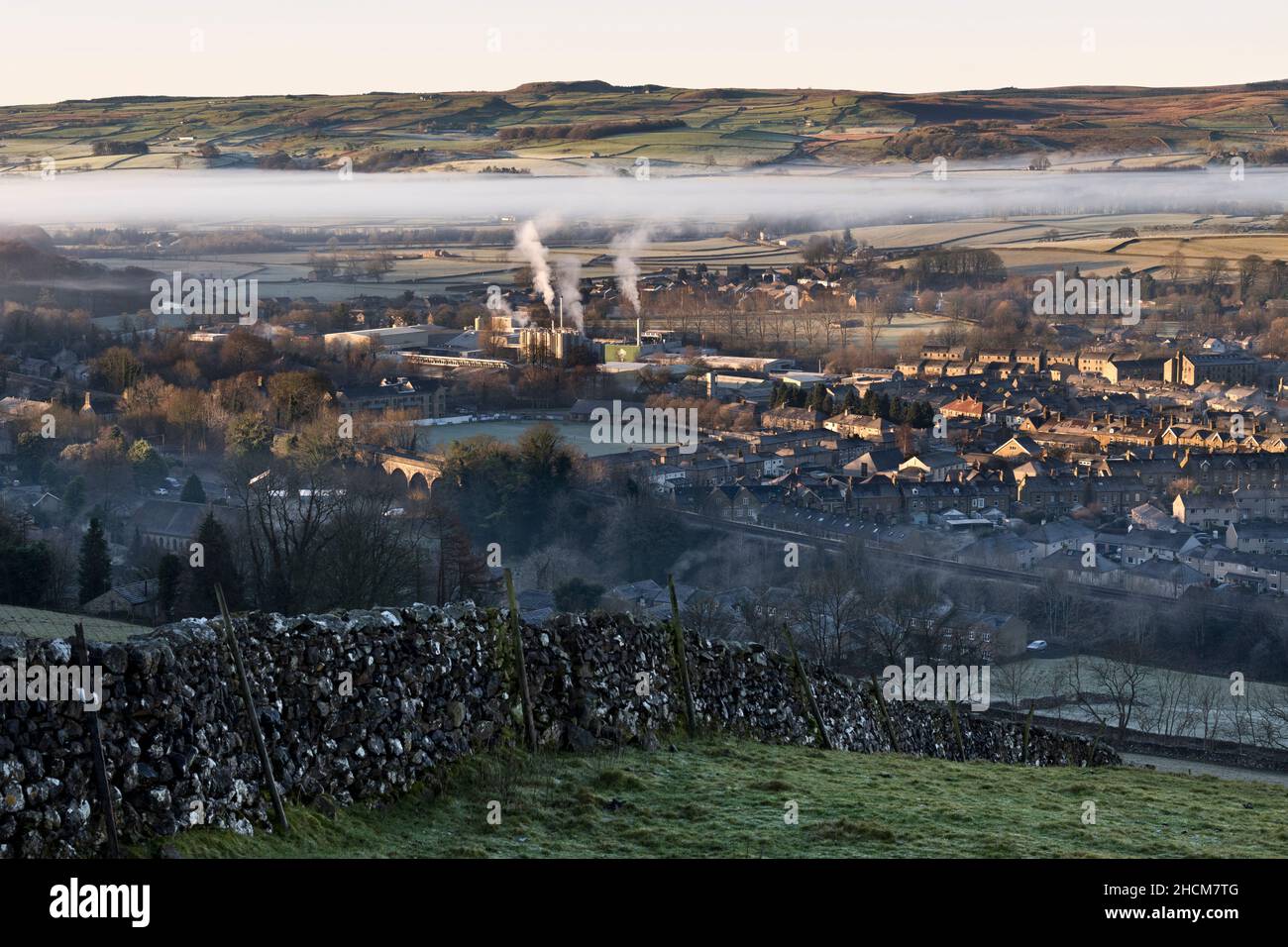 Wintertemperatur-Umkehrung, mit niedriger Wolke über der Yorkshire Dales Stadt Settle. Rauch steigt aus der siedelten Creamery (Arla Dairy) in der Mitte. Stockfoto
